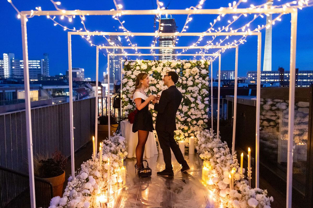 Heiratsantrag Berlin Rooftop Blumenwand Lichterketten Paar Nacht